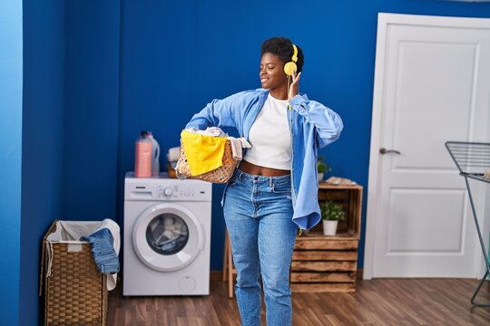 African american woman holding basket with clothes listening to music at laundry room