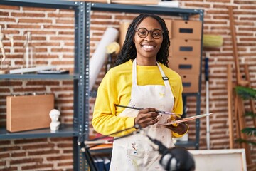 African american woman artist smiling confident holding paintbrush and palette at art studio