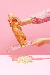 Female hands grating bread, baguette to make breadcrumb for meat isolated over pink background