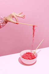 Colorful image of female hand and pink noodles isolated over pink background. Japanese cuisine, culture
