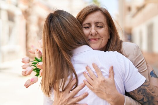 Mother and daughter hugging each other holding bouquet of flowers at street