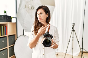 Beautiful caucasian woman working as photographer at photography studio pointing aside worried and...