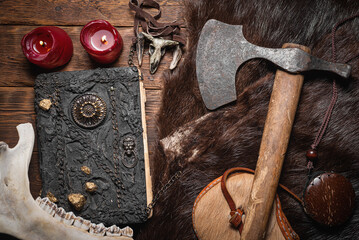 Ancient viking axe, book and beast fur skin on the old wooden table flat lay table background.