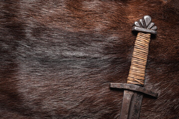 Ancient viking sword on the beast fur skin flat lat background close up.