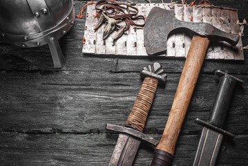 Ancient weapon, swords and axe on the black wooden table background close up.