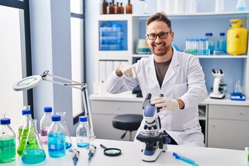 Middle age caucasian man working at scientist laboratory smiling happy pointing with hand and finger