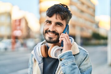 Young hispanic man talking on the smartphone wearing headphones at street