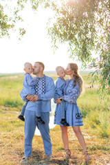 Fototapeta premium Happy parents hold their two twins sons on the hands and kiss them during walk on meadow.