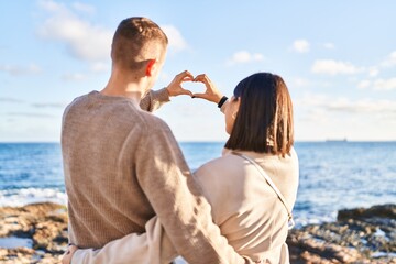 Man and woman doing heart symbol with hands on back view at seaside