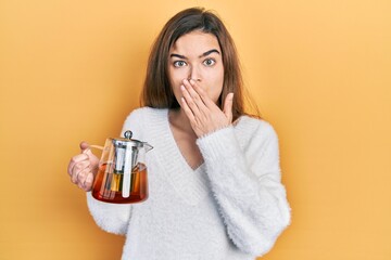 Young caucasian girl holding jar of tea covering mouth with hand, shocked and afraid for mistake. surprised expression