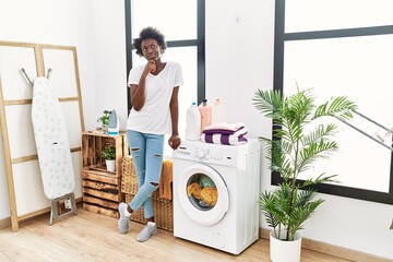 African young woman doing laundry at home serious face thinking about question with hand on chin, thoughtful about confusing idea