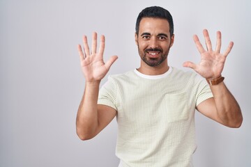 Hispanic man with beard standing over isolated background showing and pointing up with fingers number ten while smiling confident and happy.