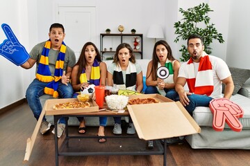 Group of young people wearing team scarf cheering football game scared and amazed with open mouth for surprise, disbelief face