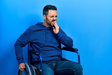 Handsome hispanic man with beard sitting on wheelchair touching mouth with hand with painful expression because of toothache or dental illness on teeth. dentist