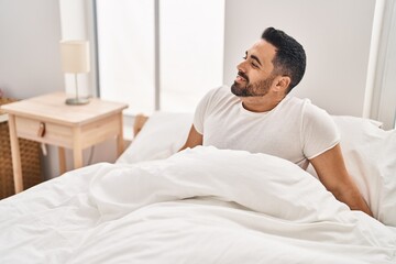 Young hispanic man smiling confident sitting on bed at bedroom