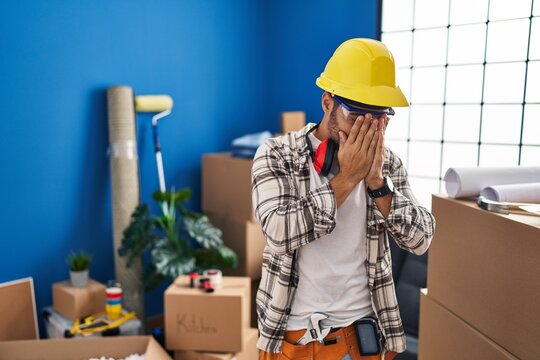 Young hispanic man with beard working at home renovation with sad expression covering face with hands while crying. depression concept.