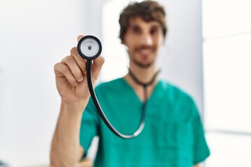 Young hispanic man wearing doctor uniform holding stethoscope at clinic