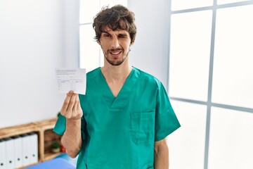 Young hispanic doctor man holding covid record card winking looking at the camera with sexy...