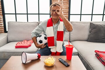 Senior man watching football holding ball supporting team smiling happy doing ok sign with hand on...