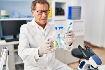 Middle age man wearing scientist uniform looking test tubes at laboratory
