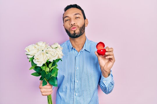 Hispanic man with beard holding bouquet of flowers and engagement ring looking at the camera blowing a kiss being lovely and sexy. love expression.