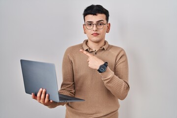 Non binary person using computer laptop pointing with hand finger to the side showing advertisement, serious and calm face