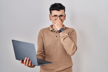 Non binary person using computer laptop smelling something stinky and disgusting, intolerable smell, holding breath with fingers on nose. bad smell