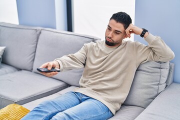 Young arab man watching tv with boring expression at home
