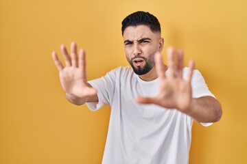 Young handsome man wearing casual t shirt over yellow background afraid and terrified with fear expression stop gesture with hands, shouting in shock. panic concept.