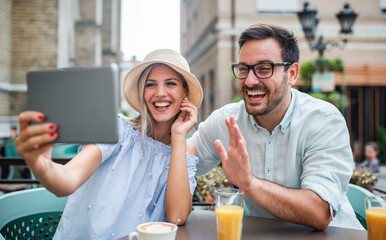 Young couple sitting in the cafe and making video call with friends via tablet. Dating, love, relationships, technology concept