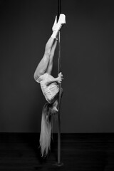 A muscular female dancer with long blonde hair is doing a Shoulder Mount move with her legs up on a...