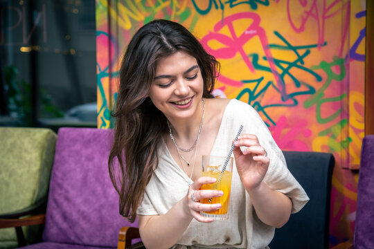 Happy young woman with a glass of lemonade against a bright painted wall.
