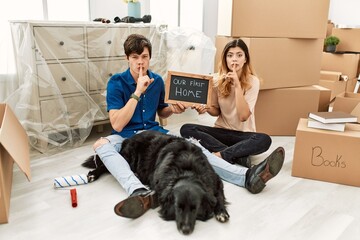 Young caucasian couple with dog holding our first home blackboard at new house asking to be quiet...