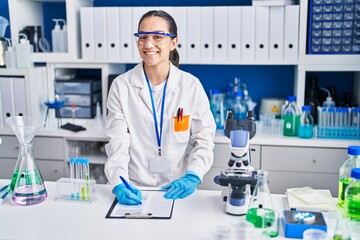 Young hispanic woman scientist writing on document working at laboratory