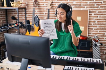 Fototapeta na wymiar Young south asian woman doing online music tutorial showing music sheet smiling with an idea or question pointing finger with happy face, number one