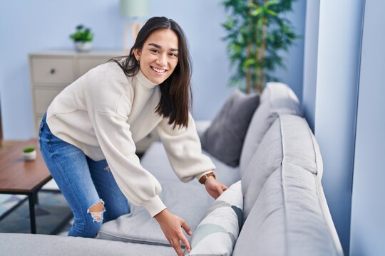 Young hispanic woman organizing sofa at home