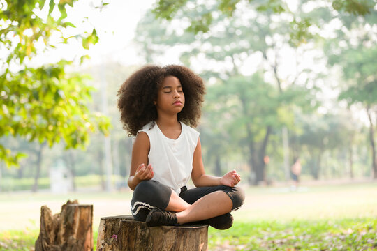 Teenager african american little girl doing meditate yoga asana with eyes closed outdoor in park. Child girl practicing doing yoga outdoor
