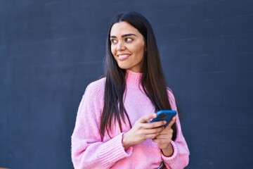 Young hispanic woman smiling confident using smartphone at street