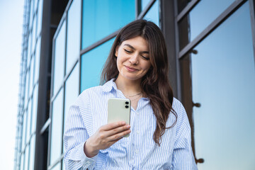 Beautiful young woman with a smartphone on the background of a glass building.