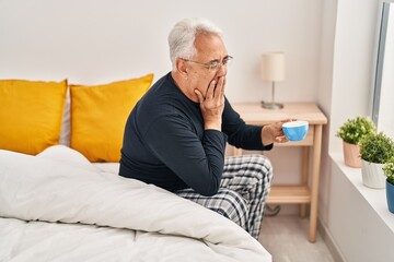 Fototapeta premium Senior man drinking cup of coffee sitting on bed at bedroom