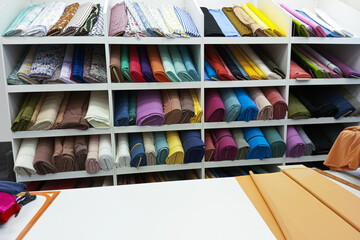 Multi-colored skeins of fabric on the shelves in  store. Table for cutting fabric.