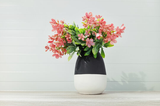 Houseplant pink flowers in vase on a shelf in the room.