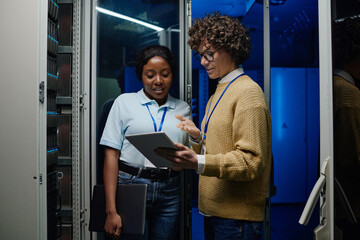 IT engineers standing beside server rack cabinet, doing wireless maintenance and diagnostics procedure with laptop