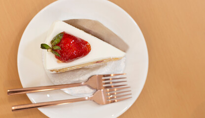 Top view of strawberry and cream sponge cake in white plate on a wooden table.