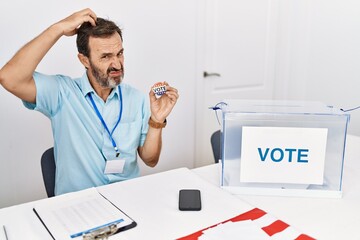 Middle age man with beard sitting by ballot holding i vote badge confuse and wondering about...