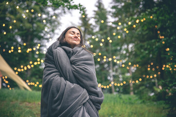 A young woman wrapped in a blanket in the forest on a blurred background.