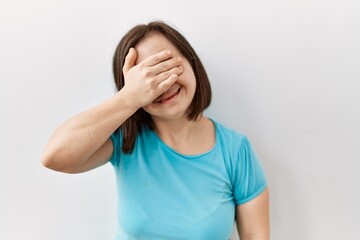 Young down syndrome woman standing over isolated background smiling and laughing with hand on face covering eyes for surprise. blind concept.