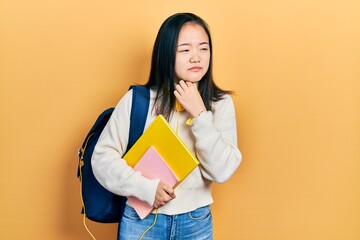 Young chinese girl holding student backpack and books touching painful neck, sore throat for flu, clod and infection