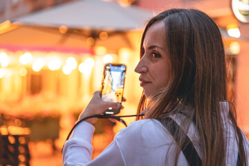 A young woman photographs a night city on a smartphone.