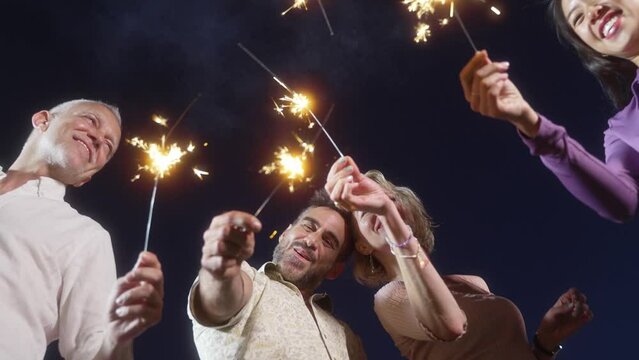 Happy mature friends having fun with sparklers at evening outdoors party in summer